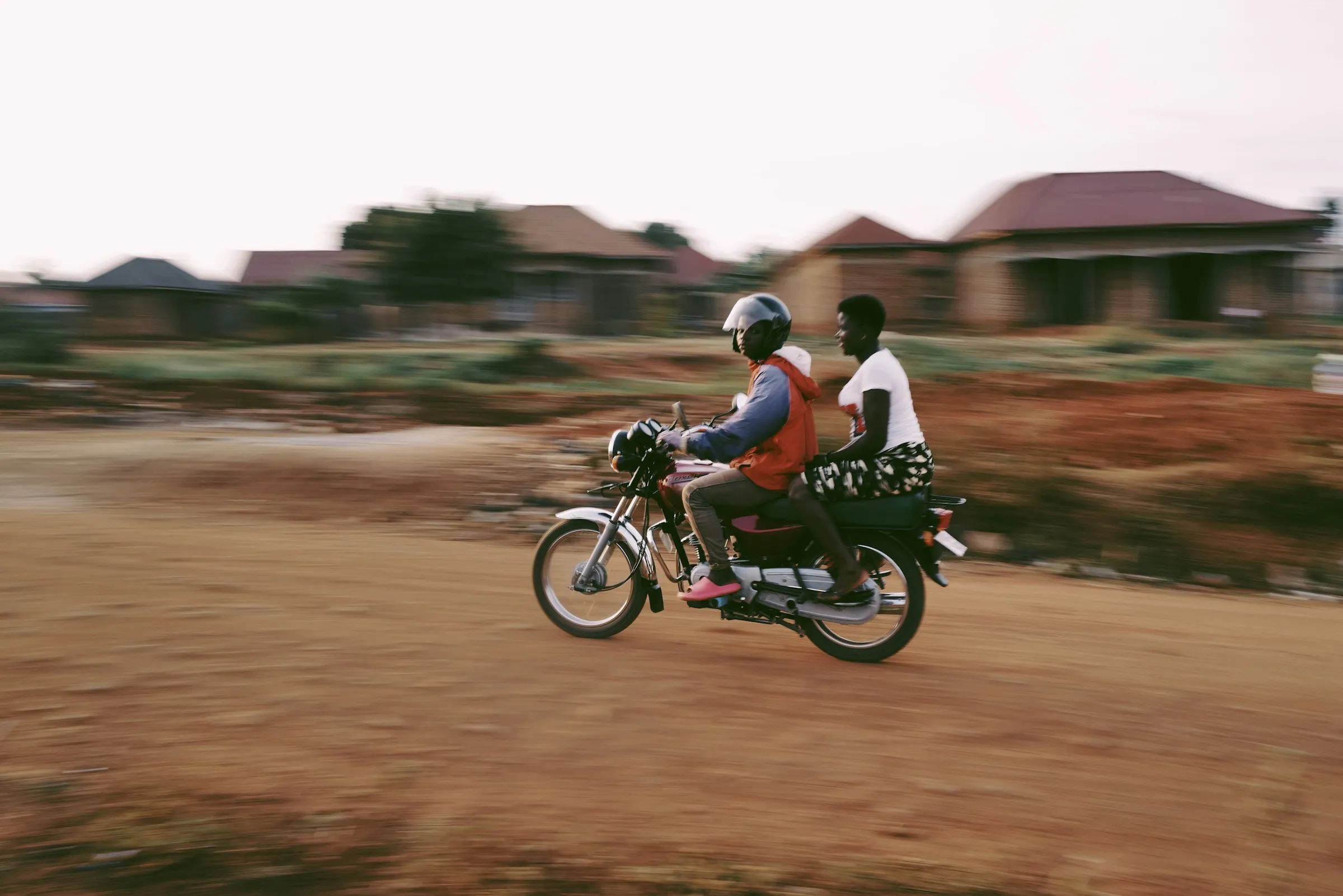 A boda boda rider carrying a passenger down a dirt road